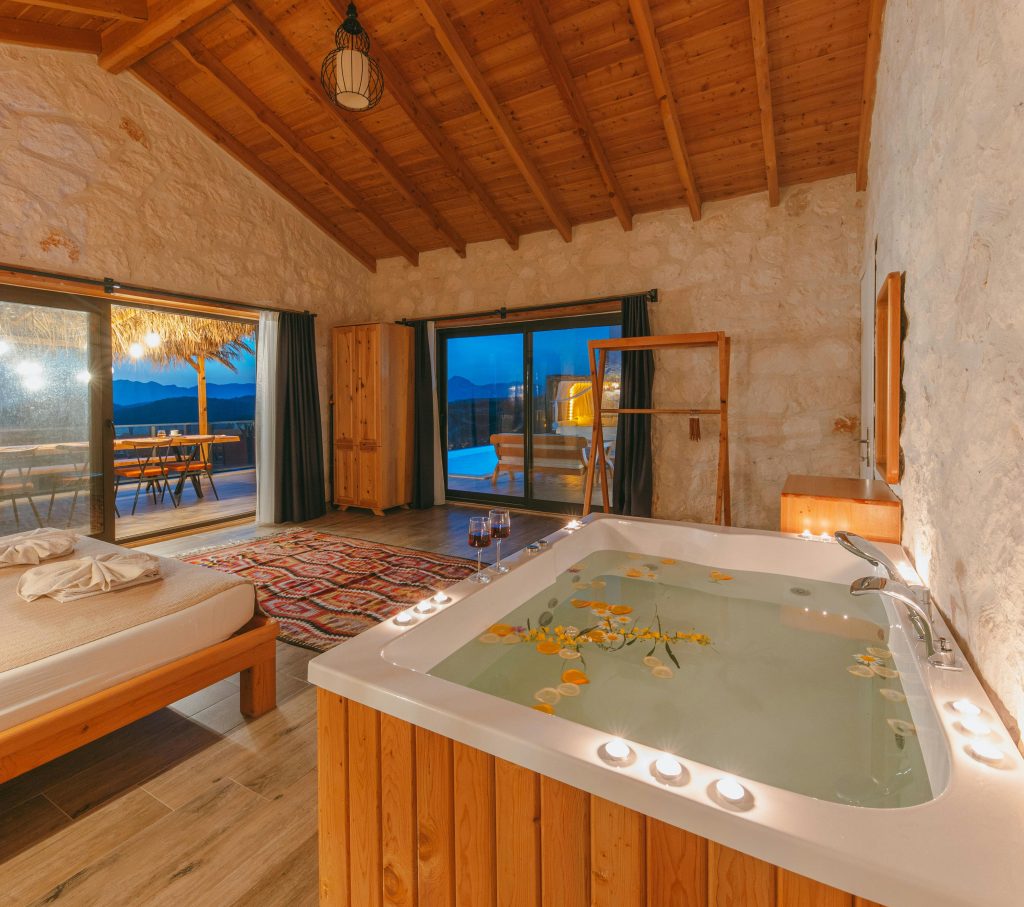 Rustic room with a private hot tub filled with petals, wooden details, soft candles, and terrace views at dusk